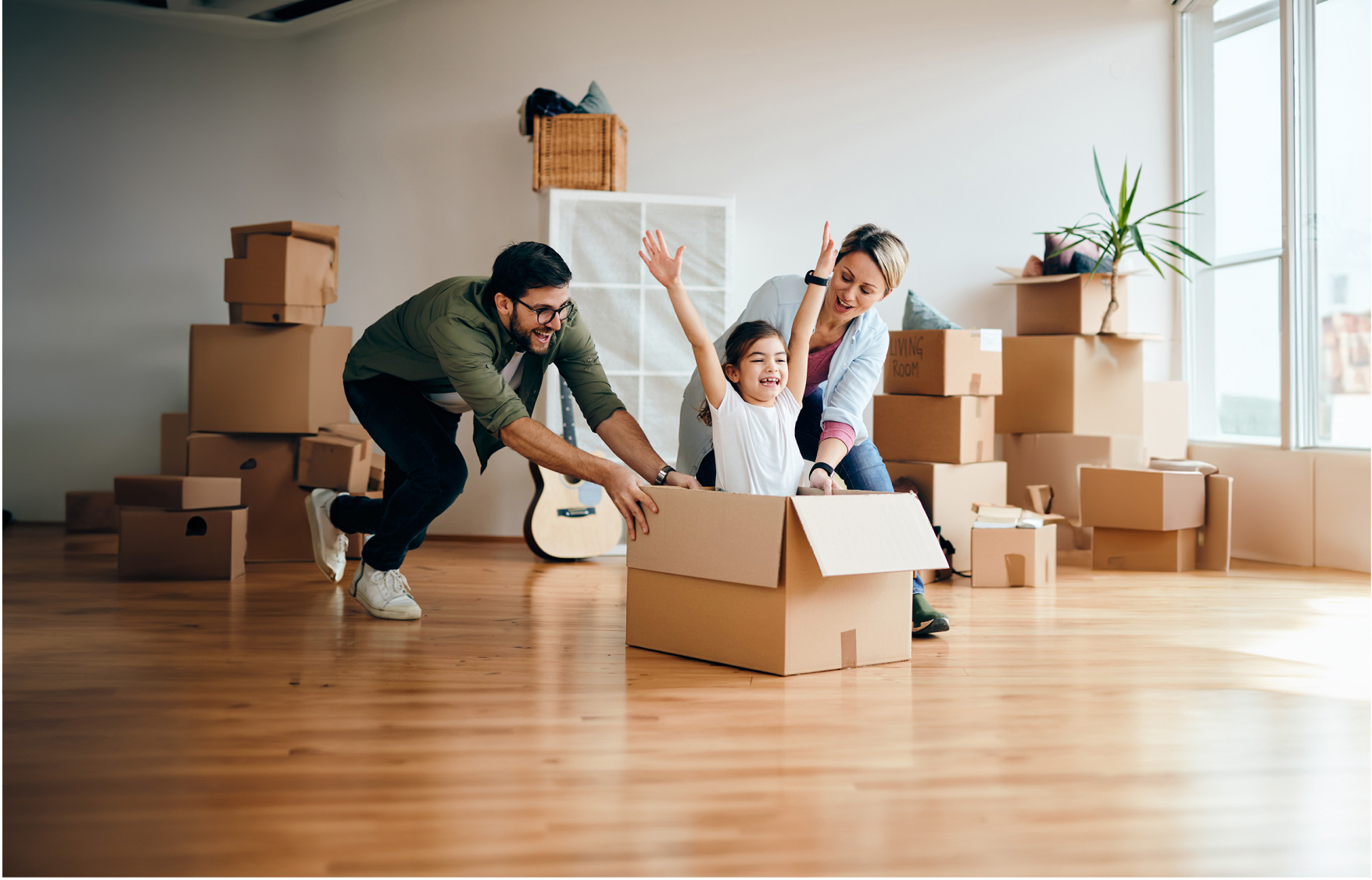 Playful parents pushing their daughter in a cardboard box in their living room