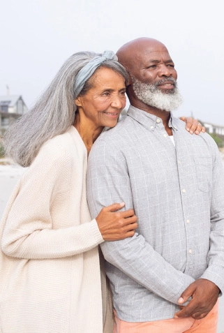 Picture of an elderly couple smiling and looking into the distance at the beach.