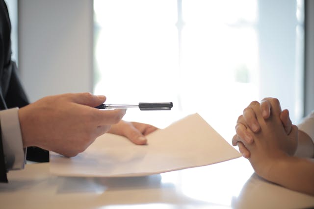 person handing paper and pen to another person